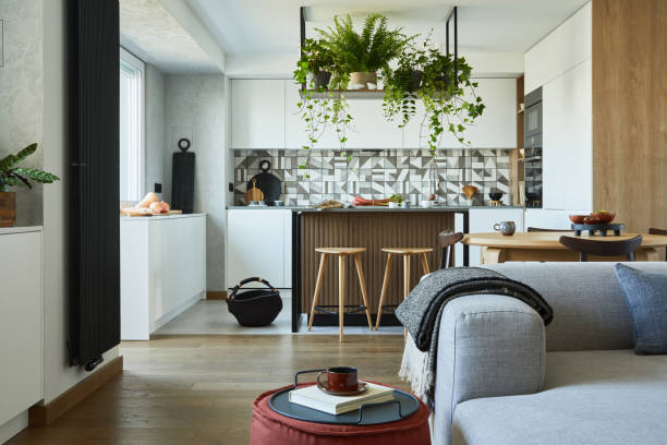 istock Stylish living room interior design with dining space, kitchen island, grey sofa. Workspace with kitchen accessories on the back ground. Creative walls with wooden panels. Minimalistic style an plant love concept. 1333170570