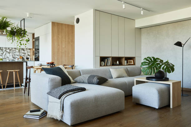 istock Stylish living room interior design with dining space, kitchen island, grey sofa. Workspace with kitchen accessories on the back ground. Creative walls with wooden panels. Minimalistic style an plant love concept. 1333170660