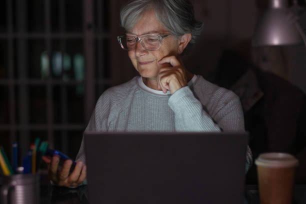 istock Senior woman looking and using laptop at home late night working watching videos on computer 1333173590