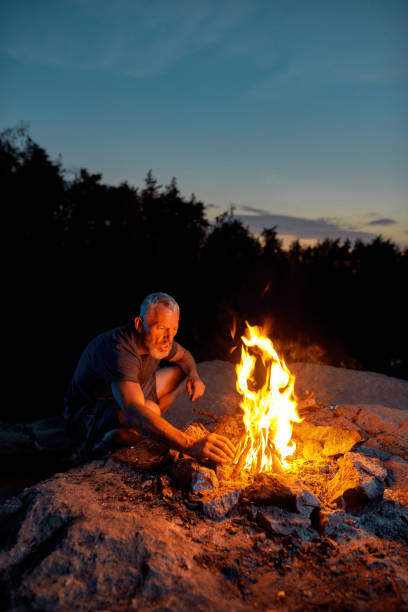istock Mature man, tourist looking busy while making a fire, spending time outdoors in forest at twilight 1333173617