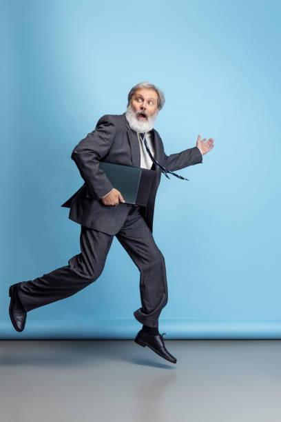 istock Scared professor, teacher, gray-headed bearded man running, hurrying to class isolated on blue studio background. Funny meme emotions 1333175287