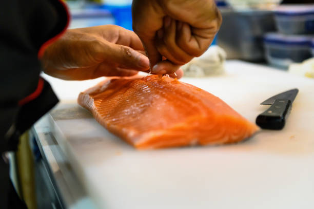 istock Fresh salmon fillet close-up on white cutting board table while fishbone removal with stainless steel tweezers 
