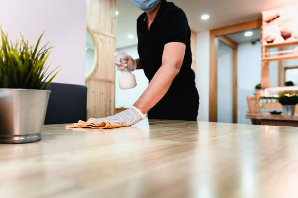 Hand of waiter woman cleaning table with disinfectant spray and microfiber cloth for disinfecting at indoor restaurant. Coronavirus prevention concept. stock photo