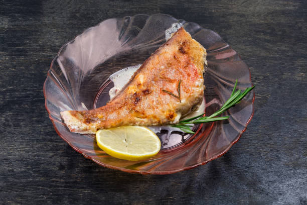 Ocean perch cooked in sour cream sauce on glass dish Ocean perch cooked in sour cream sauce on a red glass plate on a dark surface ocean perch stock pictures, royalty-free photos & images