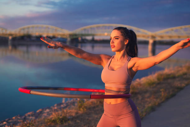 mujer joven haciendo ejercicio de hula hoop en la orilla del río - hooping fotograf�ías e imágenes de stock