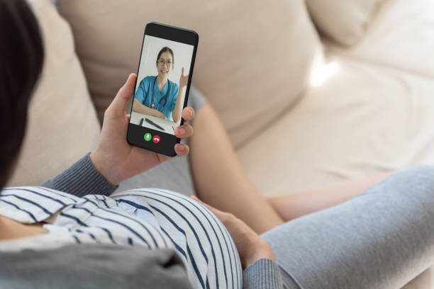 Asian pregnant woman sitting on sofa having online video chat with obstetrician doctor on smartphone at home. Asian pregnant woman sitting on sofa having online video chat with obstetrician doctor on smartphone at home. Modern communication. contacting a doctor stock pictures, royalty-free photos & images