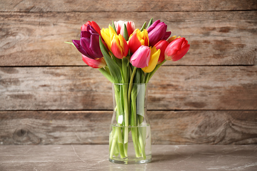 Beautiful spring tulips in vase on table against wooden background
