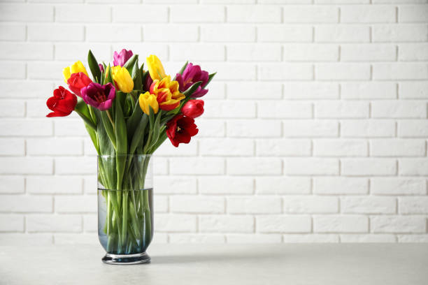 istock Beautiful spring tulips in vase on table near white brick wall. Space for text 1333185992