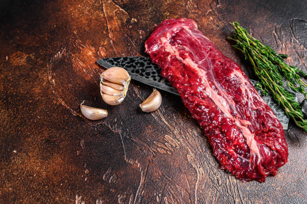 Raw organic machete or skirt steak on a butcher knife . Dark background. Top view. Copy space