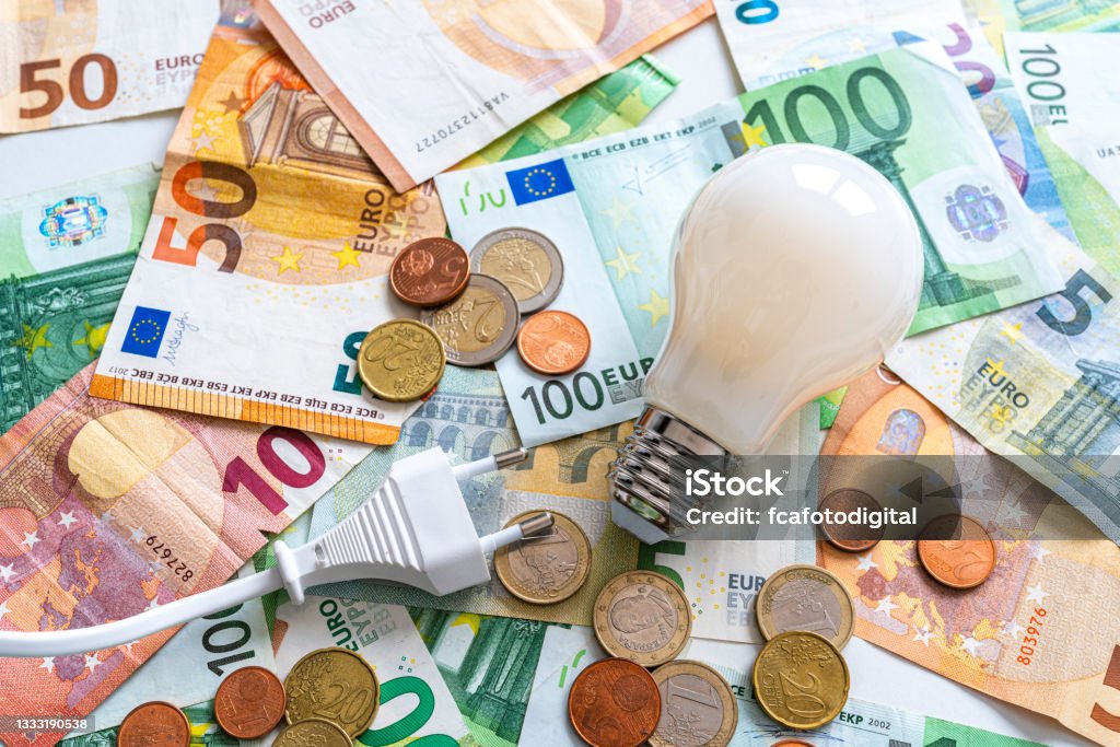 Electric plug and light bulb on Euro banknotes and coins Electricity costs: Light bulb and electric plug on Euro banknotes and coins background. High resolution 42Mp studio digital capture taken with SONY A7rII and Zeiss Batis 40mm F2.0 CF lens Fuel and Power Generation Stock Photo