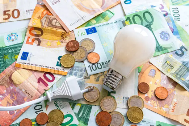 Electricity costs: Light bulb and electric plug on Euro banknotes and coins background. High resolution 42Mp studio digital capture taken with SONY A7rII and Zeiss Batis 40mm F2.0 CF lens