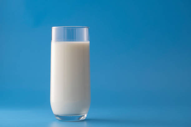 Glass of white milk isolated on blue background, close up. Dairy product concept, copy space