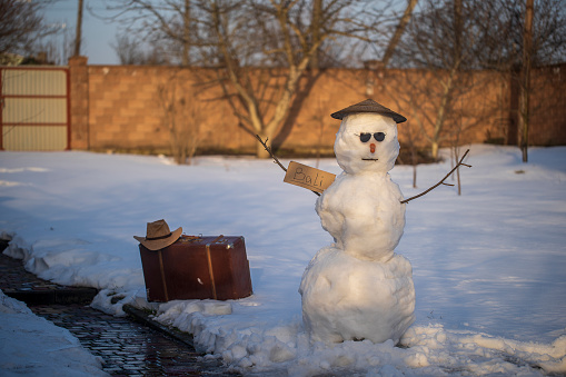 Snowman hitchhiking to Bali island in winter. Snowman catch a car by the road. Hitching a ride