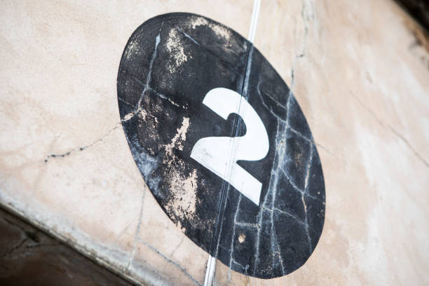 istock Number 2 in a black circle, painted onto a rough an weathered, sand-coloured wall 1333193244