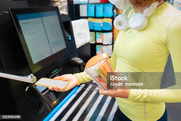 Woman Wearing Medical Mask Scans Her Supermarket Purchases At Selfservice Checkout To Make It Safer To Avoid Contact With Sellers And Cash During Covid Pandemic Stock Photo - Download Image Now