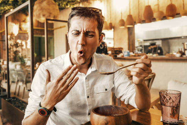 homem engraçado tenta um prato picante e quente da cozinha nacional. ele é todo vermelho e está tentando esfriar a boca com a m�ão - spice - fotografias e filmes do acervo