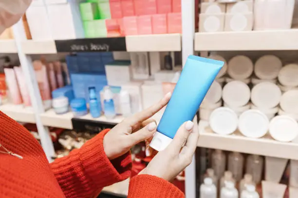 Woman customer chooses and buys cosmetics in a store or pharmacy and holds a tube of moisturizing cream or lotion in her hand