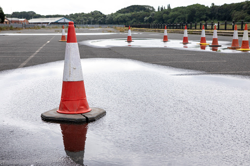 An empty parking lot with traffic cones and puddles