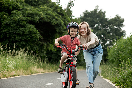 Happy Mother teaches child son to ride a bike on the bike path