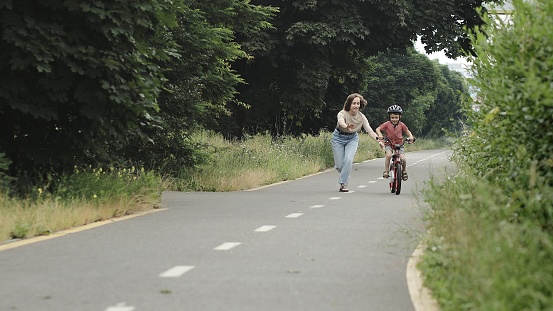 Happy Mother teaches child son to ride a bike on the bike path.