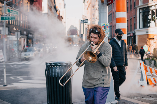 Street performer playing trumpet on Broadway. Steam chimney vent is in the background.