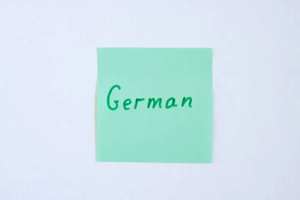 Photo of Top view flat lay of the reminder notepaper of green color with word German on it on white background. Flashcards and language studies concept