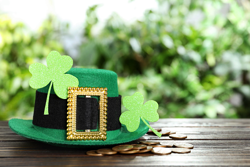 Green leprechaun hat, clover leaves and gold coins on wooden table, space for text. St Patrick's Day celebration