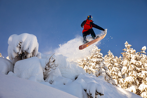 Young snowboarder at the pinnacle of a big jump in powder day