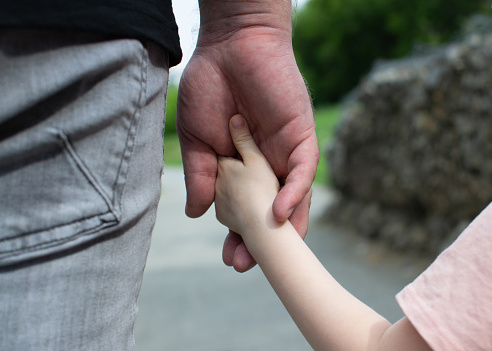 The father carefully holds the child's hand. Dad and child hold hands on a walk. Children's hand in a man's hand.