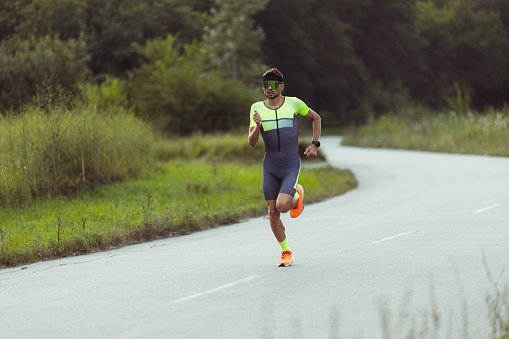 Running, jogging. Young professional male triathlete, runner training outdoors on open road. Concept of sport, lifestyle, motion and action. Copyspace for ad.