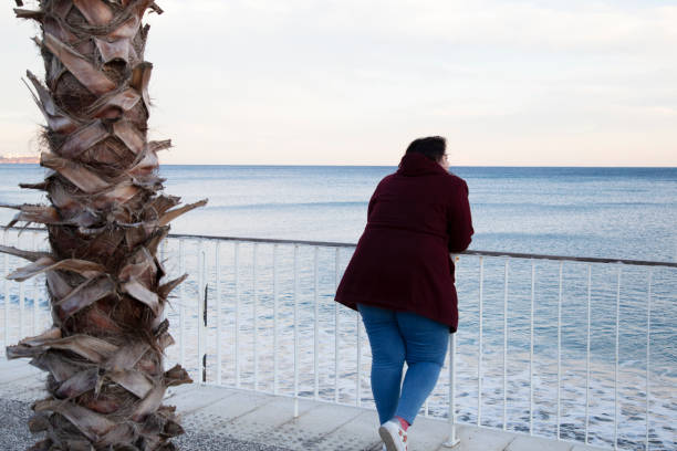 istock Young overweight woman standing alone on the beach 1333216735