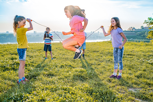 Happy school girls playing together with jumping rope outdoor