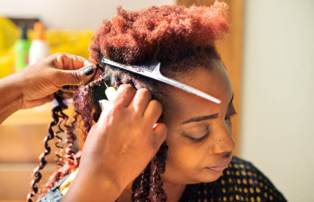 Woman getting her hair done during an appointment in a beauty salon Close-up of an African woman having her hair braided by a hairdresser during a salon appointment black woman hair extensions stock pictures, royalty-free photos & images