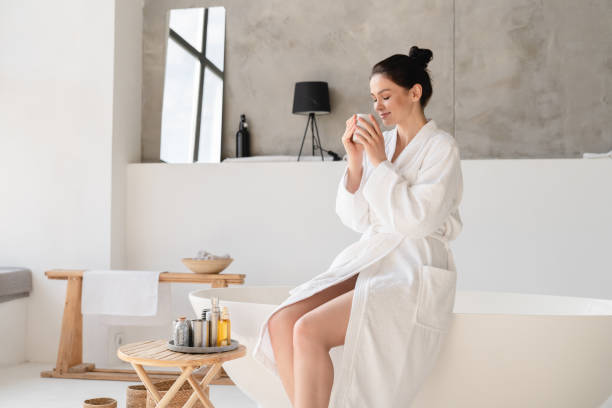 giovane bella donna che fa colazione a casa in accappatoio, preparandosi per fare il bagno nella doccia. cura del corpo e della pelle, trattamento spa di bellezza - tea women beauty pampering foto e immagini stock