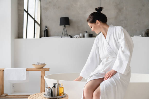 istock Good-looking young woman in spa bathrobe touching water before taking bath, preparing for shower at home. Skin and body care, recreation and serene treatment 1333222228