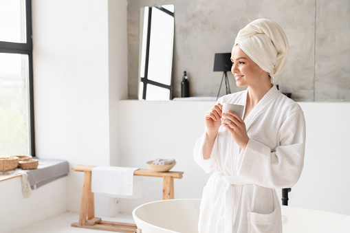 Relaxed serene young woman girl in bath spa towel and bathrobe drinking water hot beverage after shower bath at home. Stress relief concept. Beauty treatment