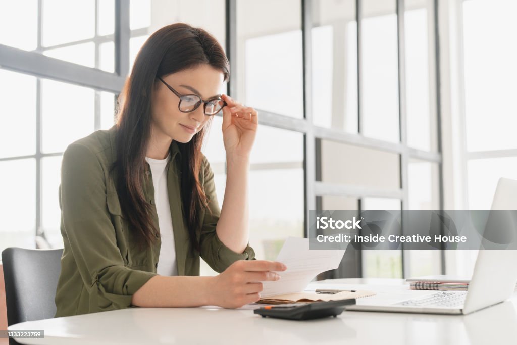 Successful young business woman freelancer manager accountant counting funds, savings, money using calculator in office. Woman paying domestic bills, economizing. Economy and finances concept Wages Stock Photo