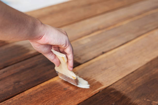 człowiek ręce gospodarstwa pędzel i farby brutto lakier na drewnianej powierzchni stołu tła. - wood stain paint deck paintbrush zdjęcia i obrazy z banku zdjęć