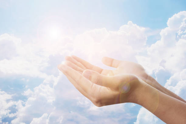 A woman raises her hands up to the sky over a white large cloud to pray and worship God. A woman raises her hands up to the sky over a white large cloud to pray and worship God. Freedom concept or Christian prayer background doing a favor stock pictures, royalty-free photos & images