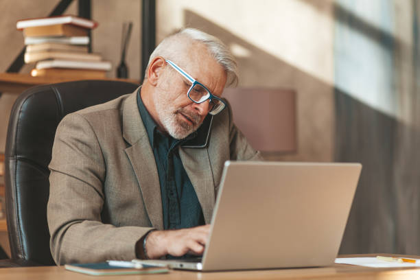 istock Busy senior man with phone at laptop. Multitasking at work 1333231572