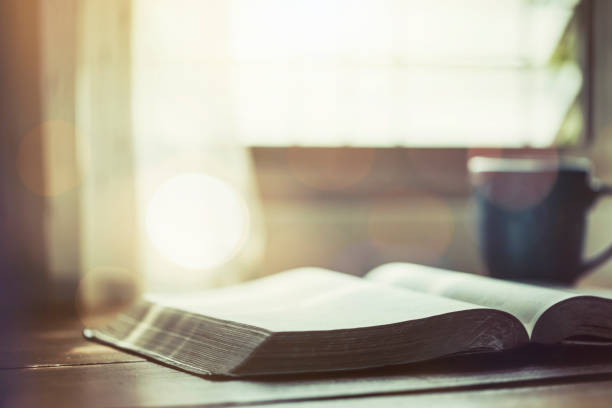 biblia abierta con una taza de café en una mesa de madera cerca de la ventana, concepto de devoción matutina - biblia fotografías e imágenes de stock