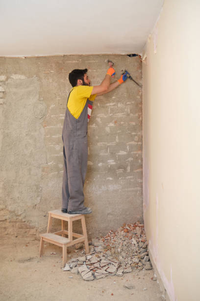 istock Young builder breaking up a house wall with a hammer and a chisel. 1333236314