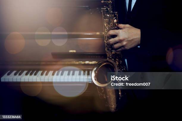 Musician Plays Alto Saxophone Over Piano With Bokeh Light Background Stock Photo - Download Image Now