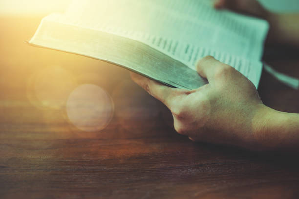 istock A man holding and read a book on a wood table with window  light, crisis solution pray to God, Christian believe, trust and obey, morning devotional concept with copy space 1333237351