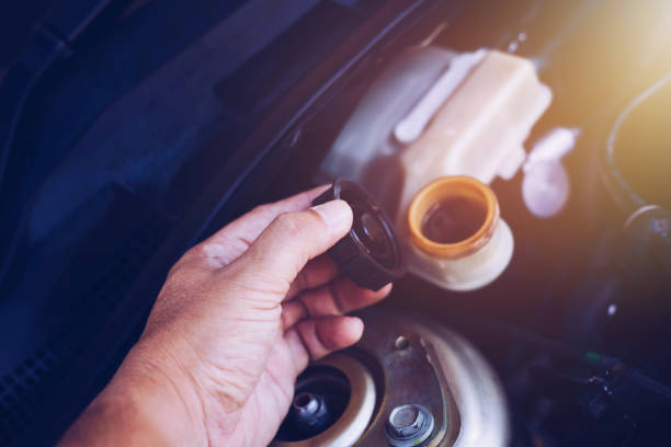 close up of man hand holding cap of  brake  fluid reservoir tank while checking brake  fluid level in an engine stock photo