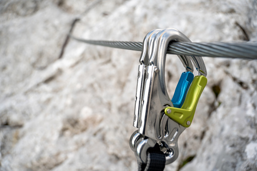 Via ferrata set with colorful carabiner hook hangs on a wire rope on a rocky mountain.