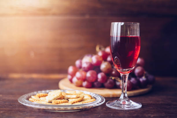 Close-up of a wine glasses with bread in communion plate  over grape on wood plate against window light  on wooden table stock photo