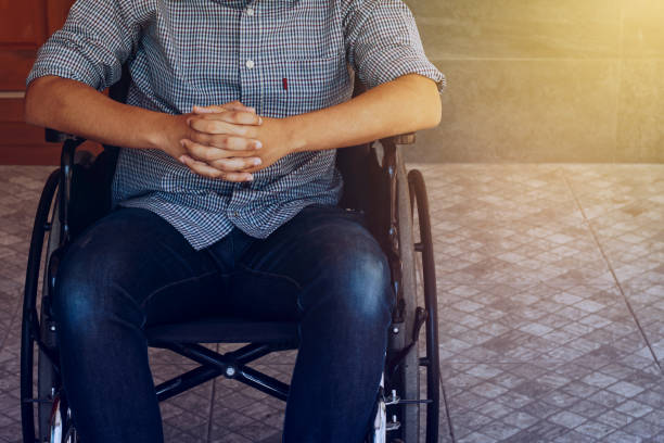 mani di un giovane che prega nella sua sedia a rotelle sul pavimento di cemento - disablement foto e immagini stock