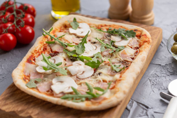 istock Rectangular pizza with mushrooms, tomatoes and arugula on a wooden cutting board 1333240746