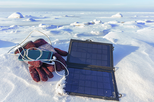 Charging mobile phone from portable tourist solar panel in winter, in cold conditions. Autonomous electric power source